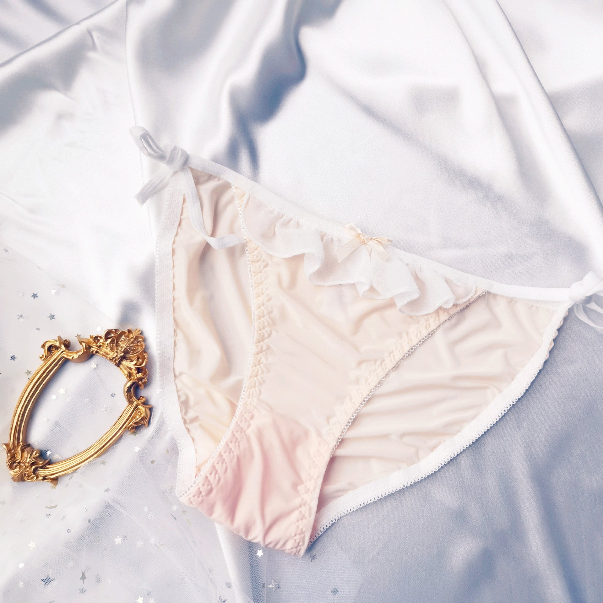 Flat lay top view of pastel pink Lolita maid lace-up panties with soft white ruffle trim and delicate bow – cute feminine femboy lingerie fashion