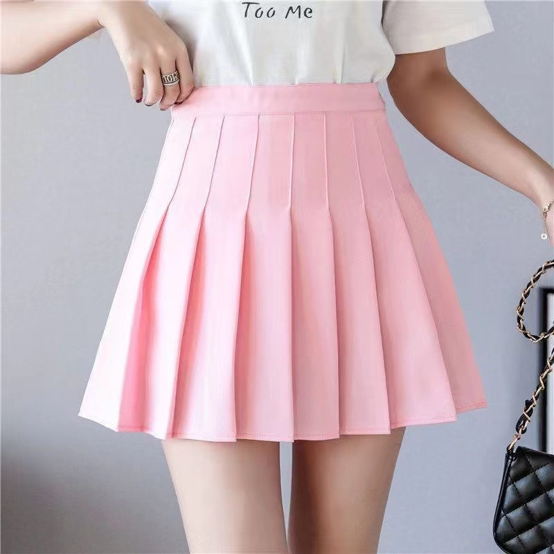 A model showcasing a pink pleated skirt paired with a white tee, set in a minimal indoor space. The vibrant pink color adds a playful touch, making this skirt a standout piece for those looking to create bold femboy outfits and explore colorful femboy fashion trends.