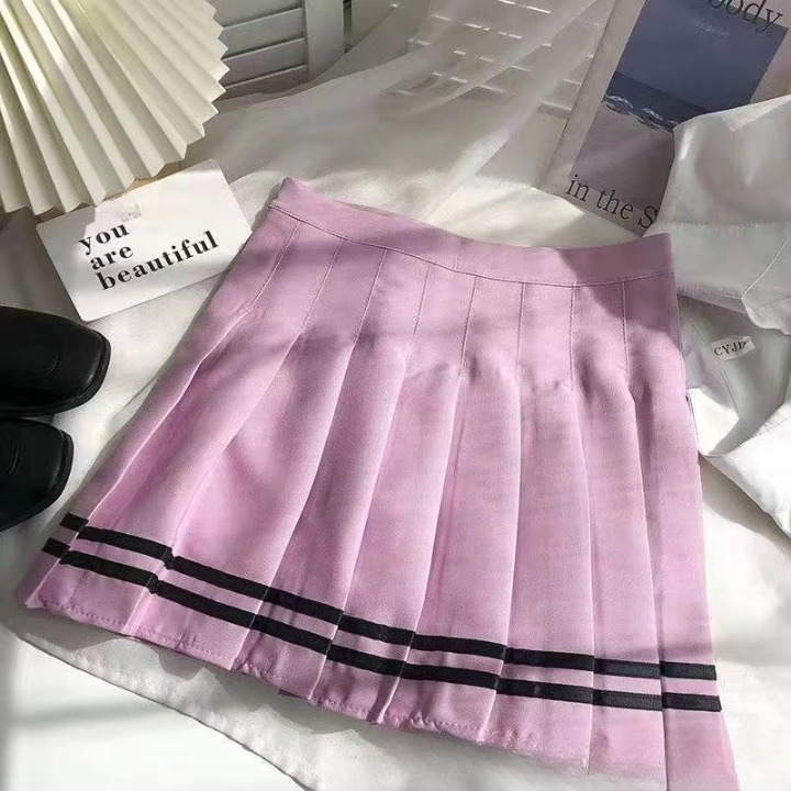 A pastel pink pleated skirt with black stripe detailing, placed in a soft indoor lighting setting. This close-up emphasizes the chic and playful design, appealing to femboy fashion fans seeking cute femboy clothing and stylish femboy outfits.