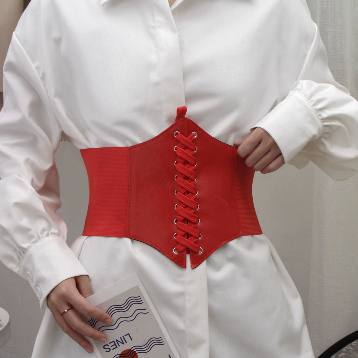 Close-up of a vibrant red corset-style waist belt with lace-up front, worn over a white shirt for a chic and bold look. Ideal for femboy fashion, adding an eye-catching element to femboy outfits.