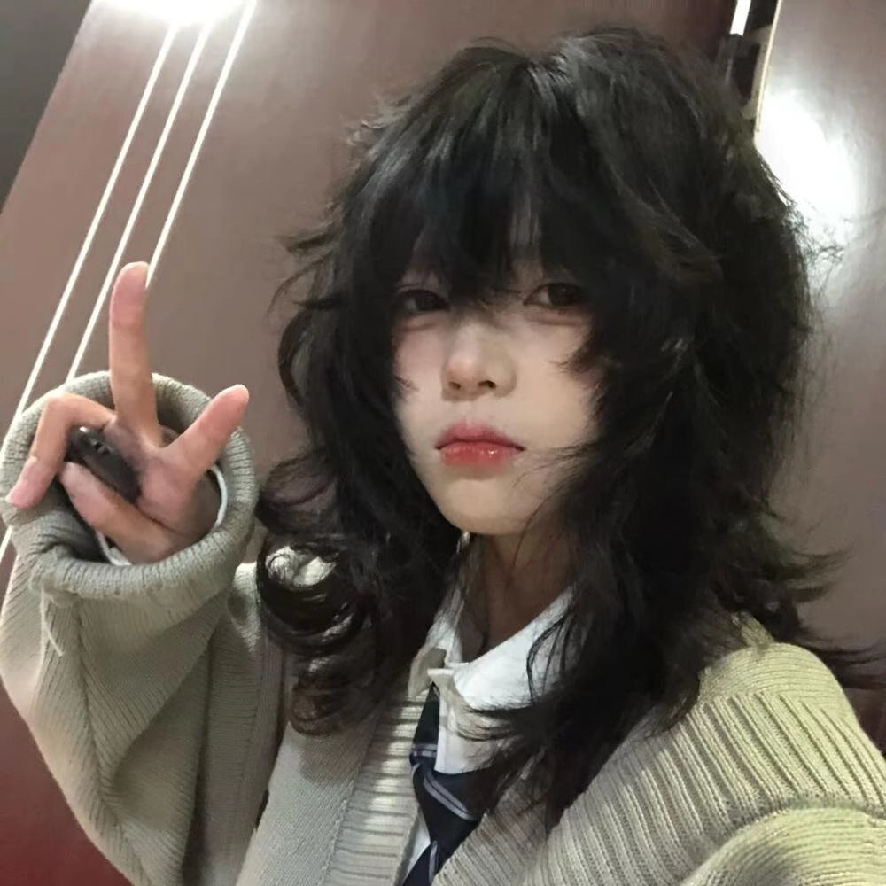 Casual selfie angle showing a soft wave wolf femboy wig with tousled layered waves and airy bangs, presenting a relaxed and cute femboy aesthetic with natural movement and soft volume in black synthetic hair.