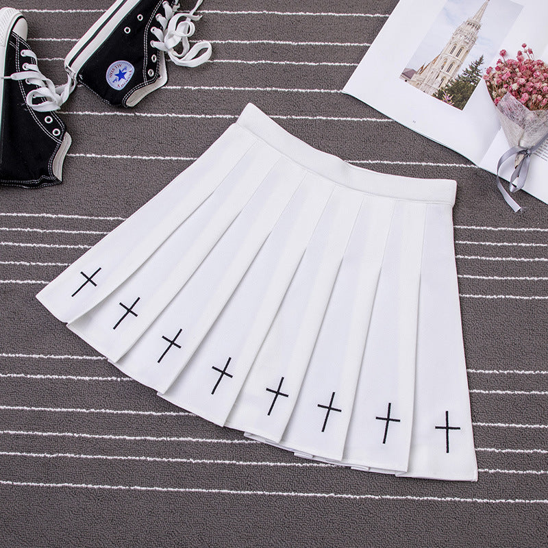 White Gothic Cross Pleated Skirt displayed on a striped carpet, emphasizing its bold cross patterns and femboy fashion trend.