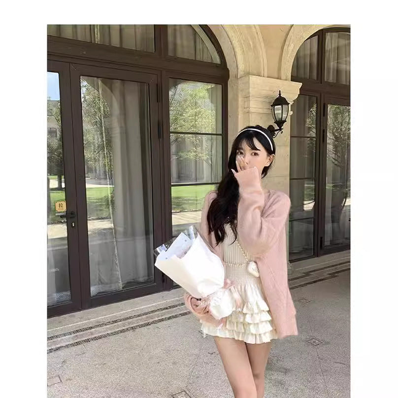 Full-body shot of a white High-Waist Cake Skirt styled with a pink cardigan and white top. Captured outdoors near a classical archway, showcasing playful and feminine femboy clothing and femboy fashion.