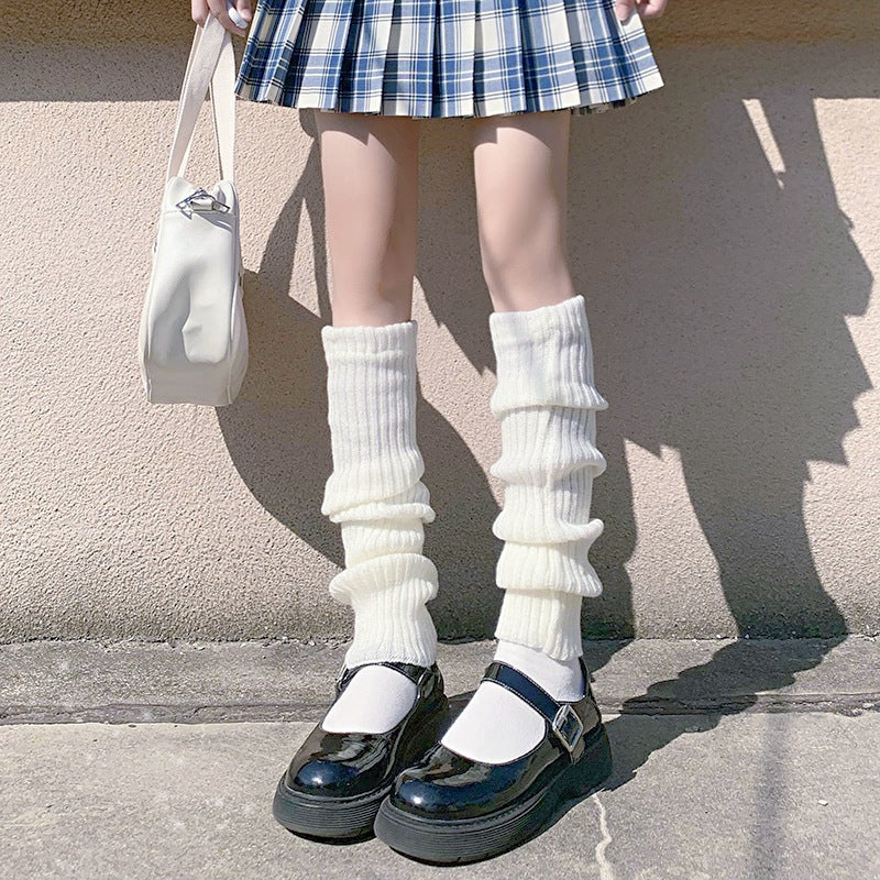White knitted leg warmers layered over socks with platform Mary Jane shoes and pleated skirt, clean lower-body composition, bright natural lighting, cute femboy outfit styling.