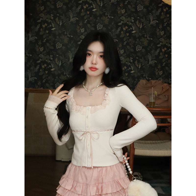 Medium shot of a white Lace Cardigan Top with lace trim and button-down details, styled with a pink ruffled skirt. Photographed indoors with a dark floral background, perfect for femboy outfits and femboy fashion.

