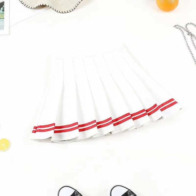 A laid-flat white pleated skirt with bold red stripes at the hem, styled in a top-down shot on a white background. The minimalist setting includes a straw hat and casual sneakers, emphasizing a playful femboy outfit perfect for a day out.